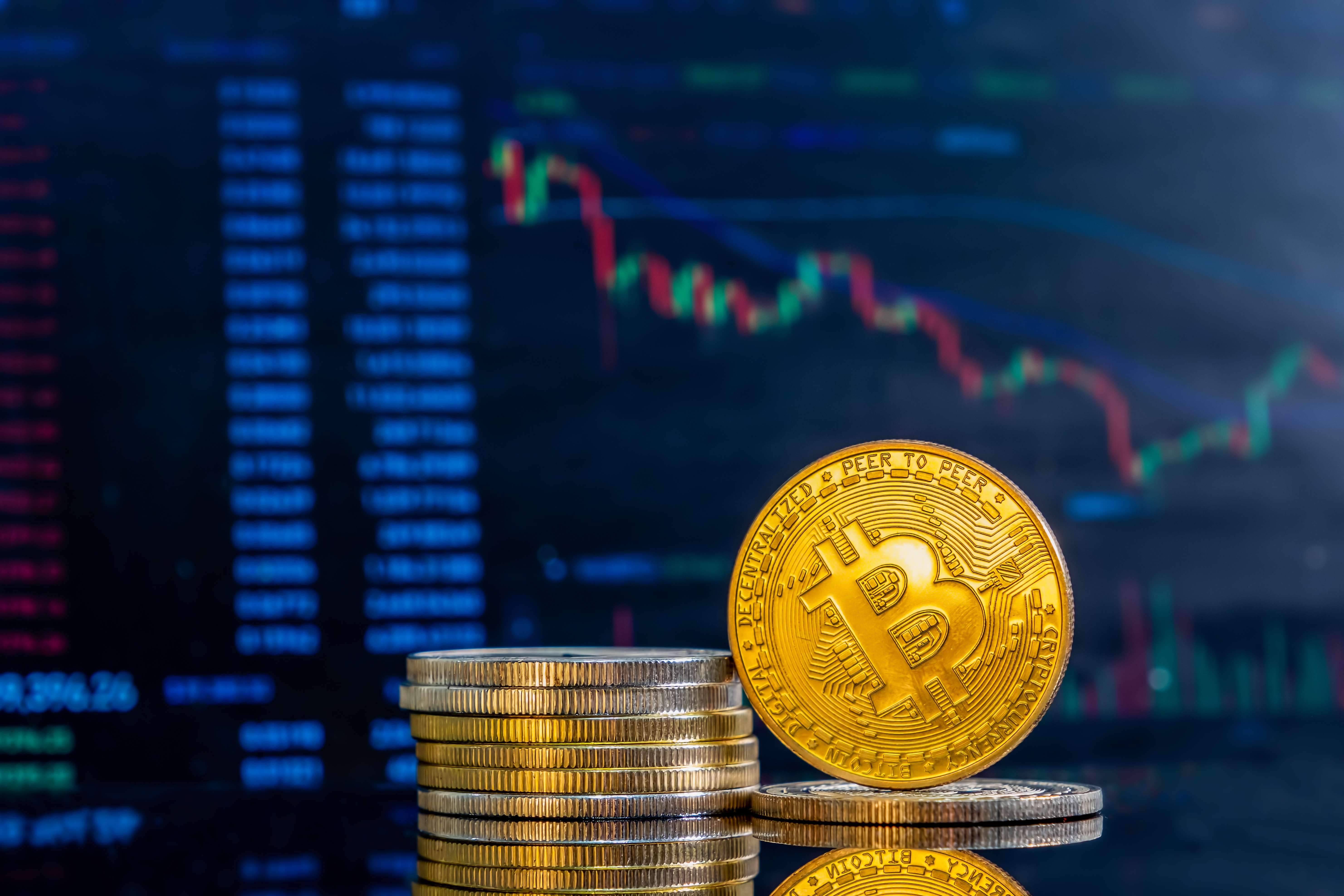 Close-up of stacked golden Bitcoin coins on a reflective surface with a cryptocurrency trading chart in the background, symbolizing market trends and daily trading cryptocurrency.